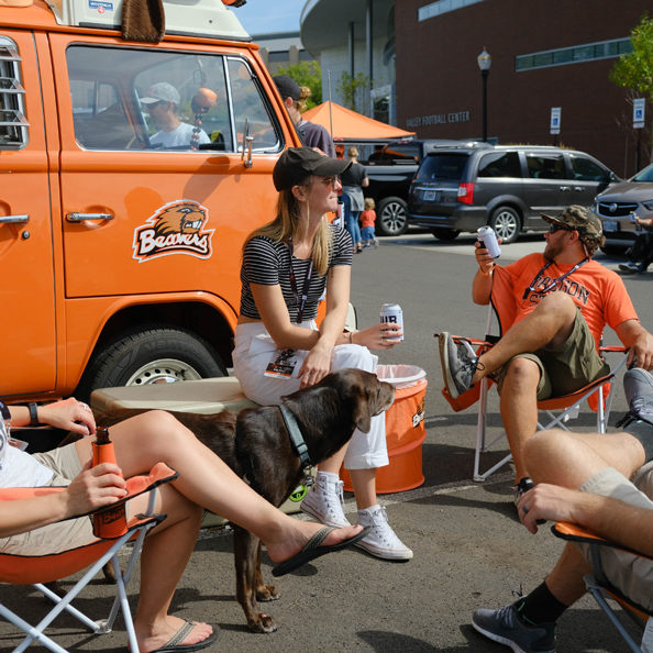 four people sitting in camp chairs next to a van with Oregon State Beavers logo on door
