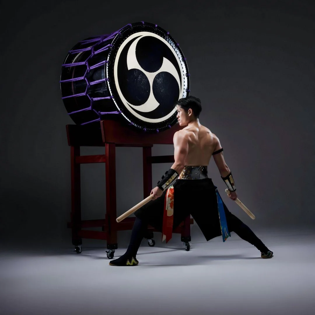 Muscular Taiko drummer lunges in front of taiko drum.