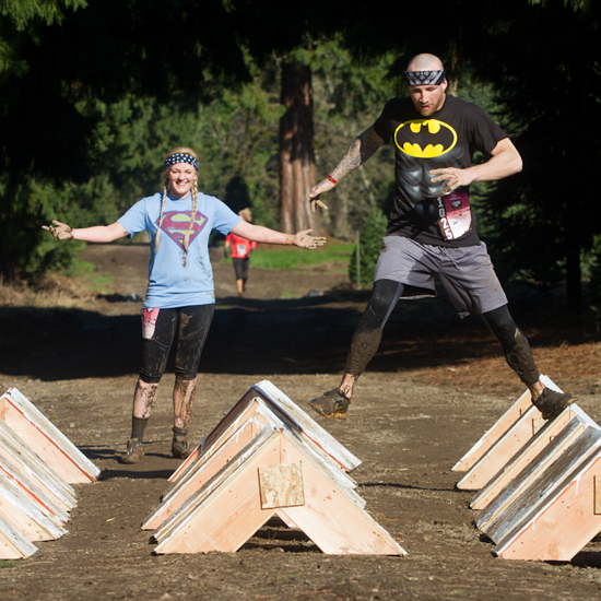 two teammates compete in obstacle course one wears a Superman logo t-shirt, the other a Batman logo tshirt