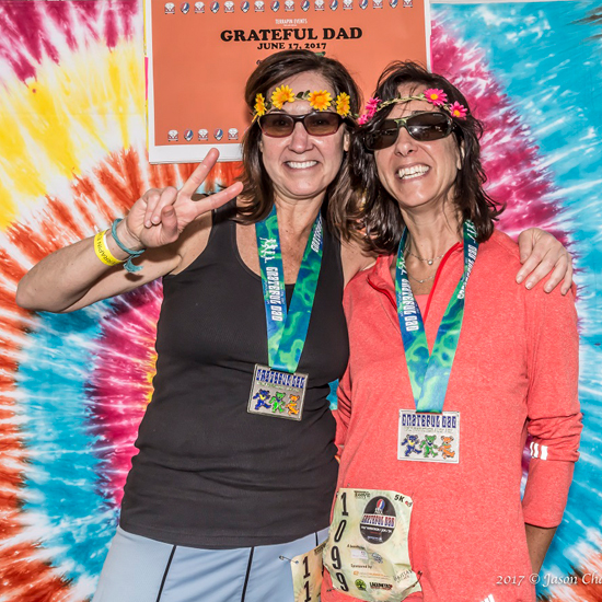 two runners pose wearing their medals in front of tie dyed backdrop