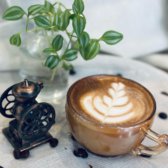cortado with latte art in clear mug in front of plant