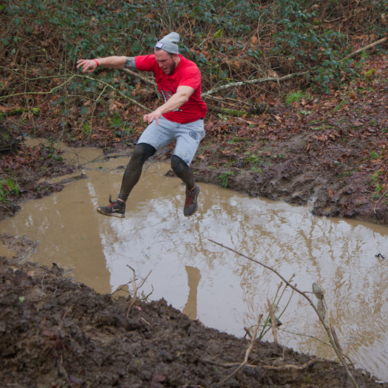 person leaping over muddy water