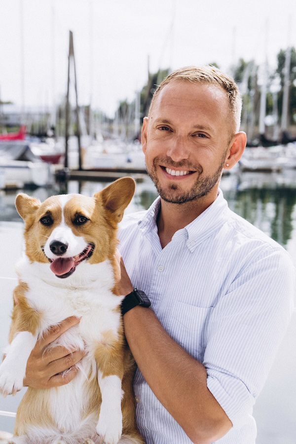 Man smiles while holding corgi in his arms.