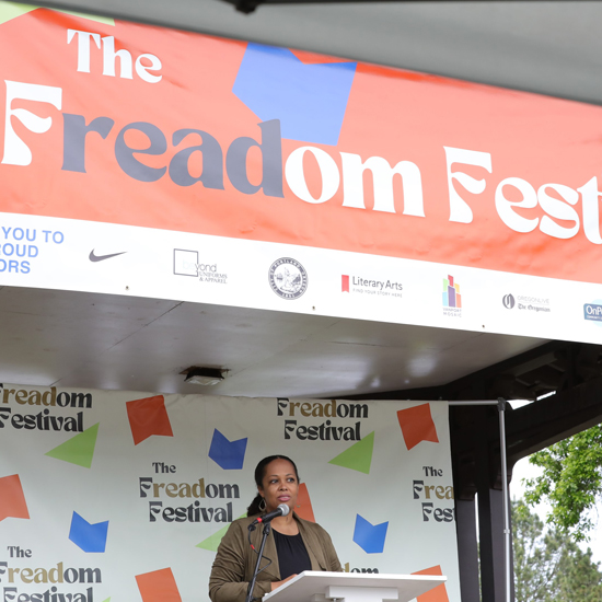 person speaks at a podium with backdrop for The Freadom Festival