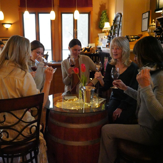 four people seated around table holding glasses of red wine