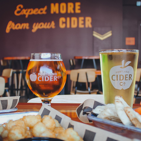 food and cider displayed on table in front of wall with 'Expect More from your cider' painted on the wall in background