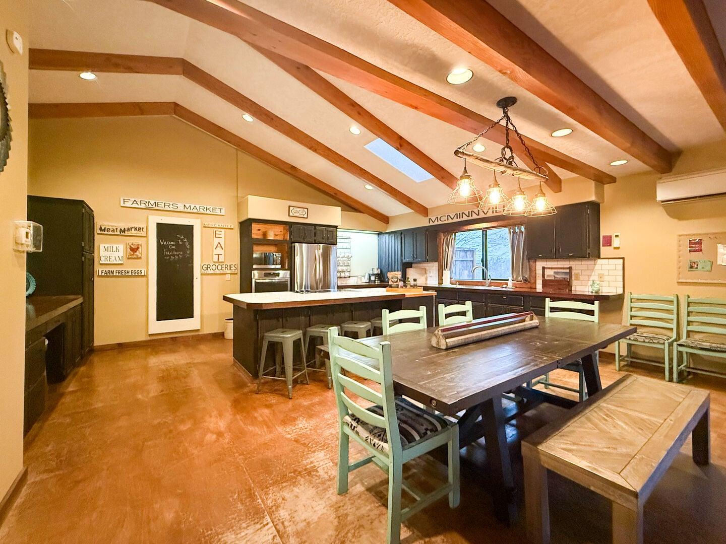 Spacious kitchen and dining area with wooden ceiling beams, dark wood dining table with green chairs, and an island with stools.