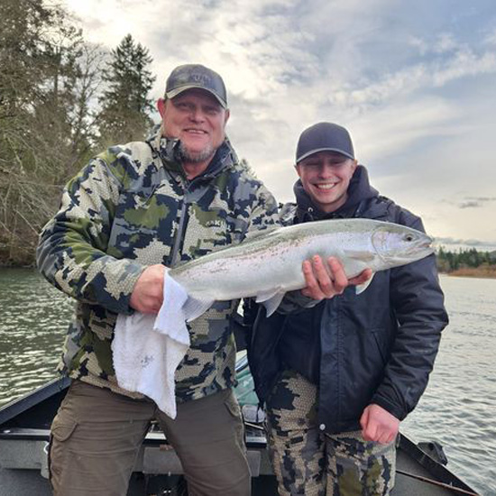 father and son smile while holding a freshly caught fish