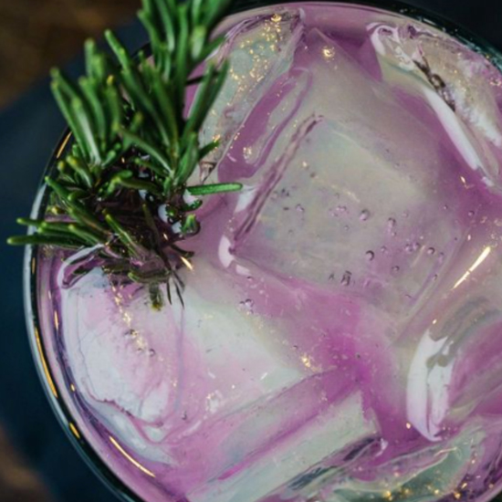 purple cocktail with ice and sprig of herbs from above