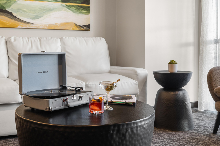 sitting area of hotel guest room with record player and two cocktails atop a round table