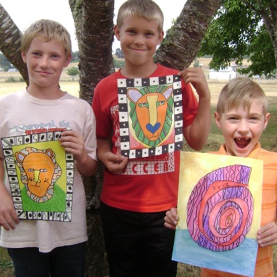 three smiling children hold up drawings