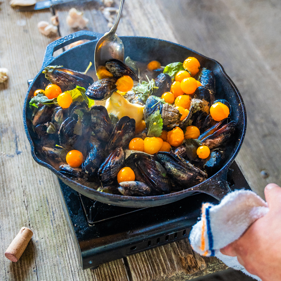 mussels and tomatoes in cast iron skillet on hot plate