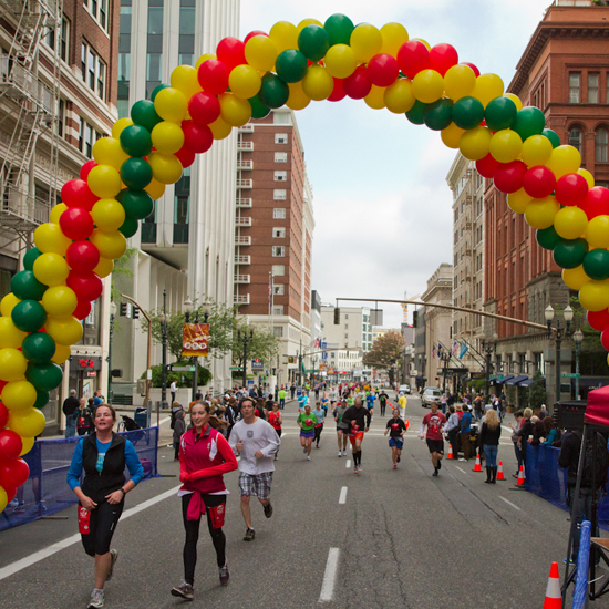 runners cross the finish line under a balloon arch