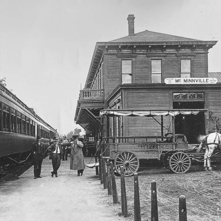 historic photo of McMinnville building with horse and cart in front and train next to it
