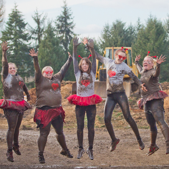 five people jump into the air after completing a muddy obstacle course