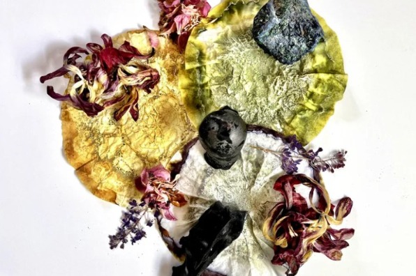 Artistic arrangement featuring three textured circular leaves in yellow, green, and white hues, each adorned with dried flowers and small dark stones.