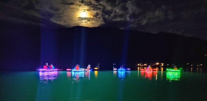 group of kayakers in light up kayaks paddle a lake at night