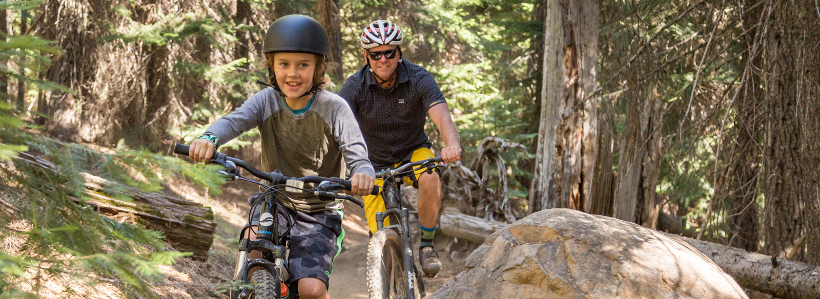 Man and boy biking in forest, smiling.