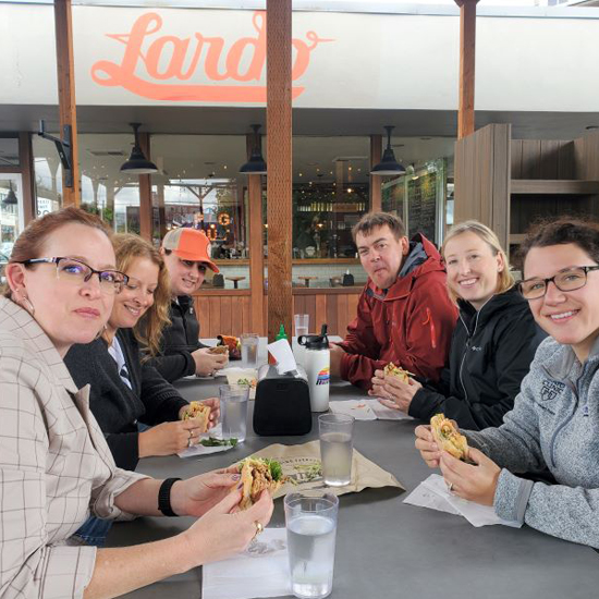 six people sit at table holding sandwiches