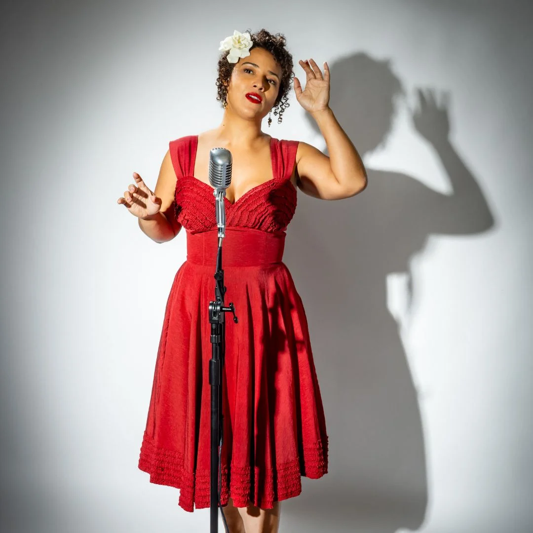 Woman wearing read dress stands behind vintage microphone.