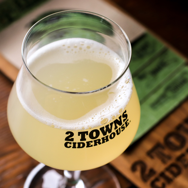 close up of cider in stemmed glass with 2 Towns Ciderhouse printed on it