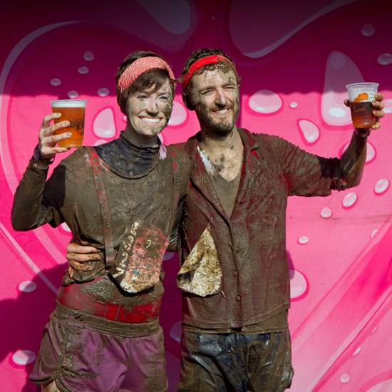 Two people covered in mud and holding a pint of beer smile for camera