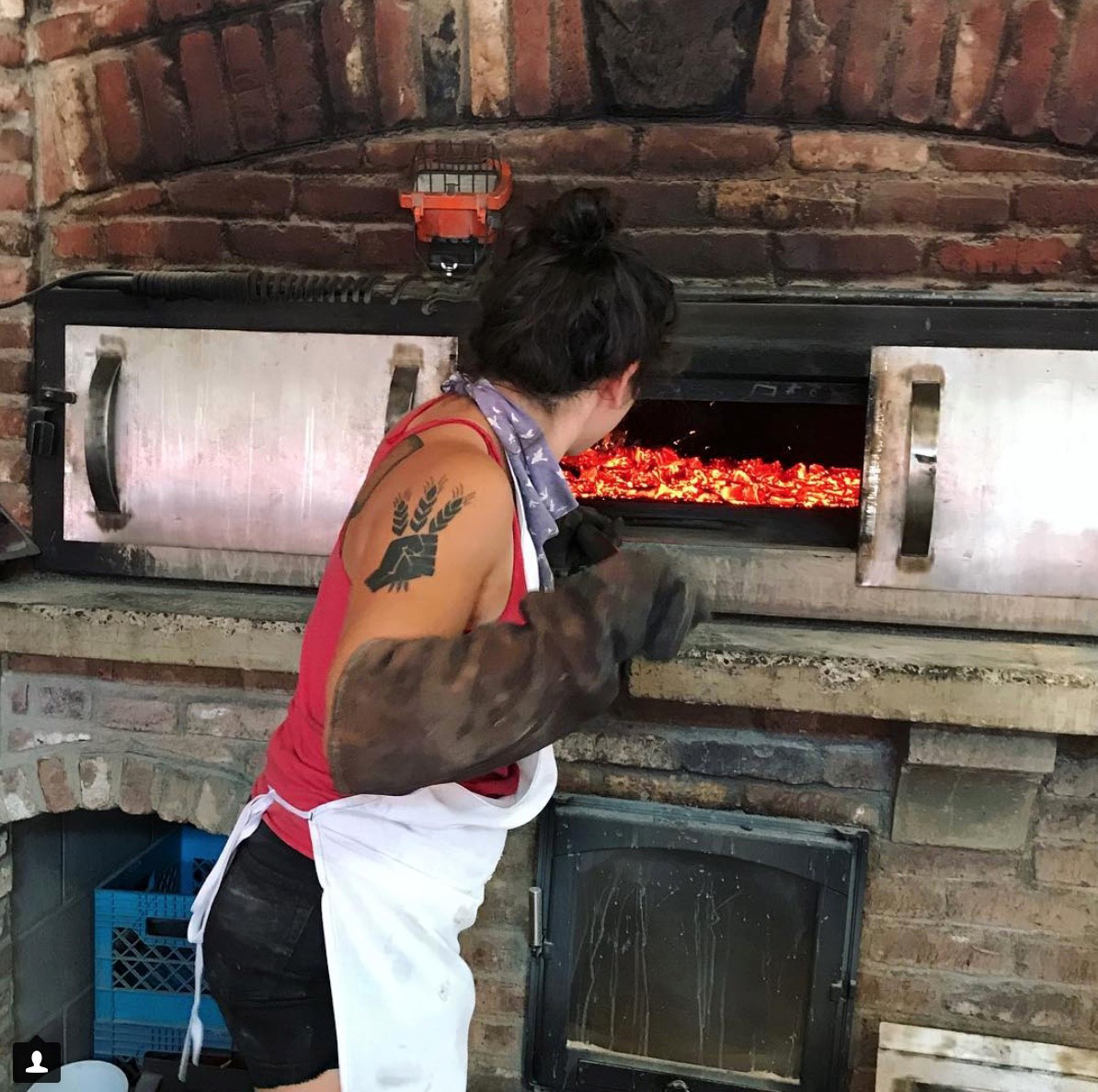 Woman with tattoo working in a brick oven.