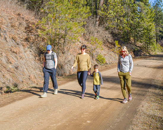 Three adults and one child walk on a gravel trail in a wooded area.