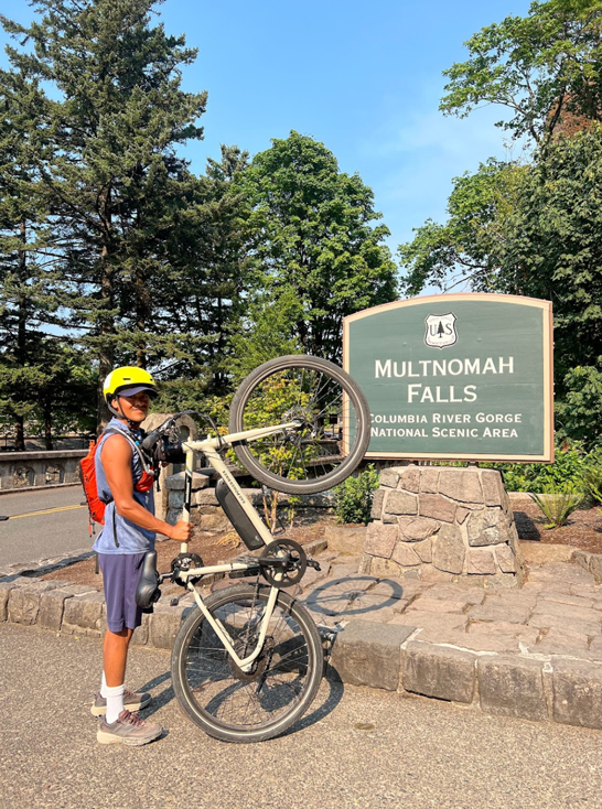 person holds bike on end at sign for Multnomah Falls