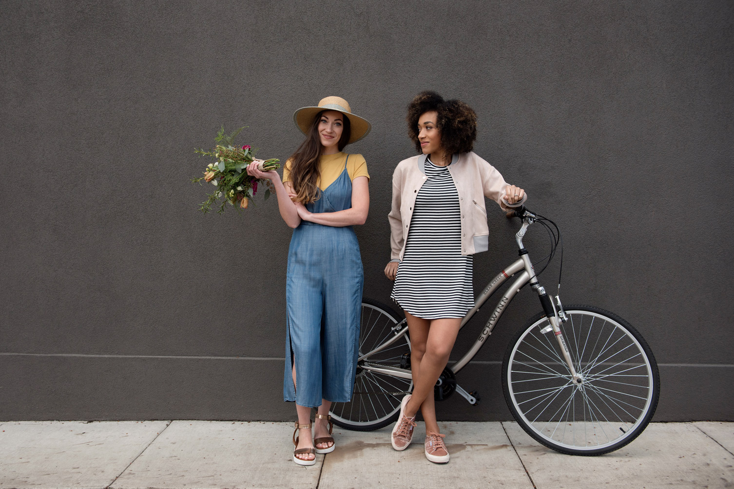 Two women standing next to a bicycle, one holding flowers.