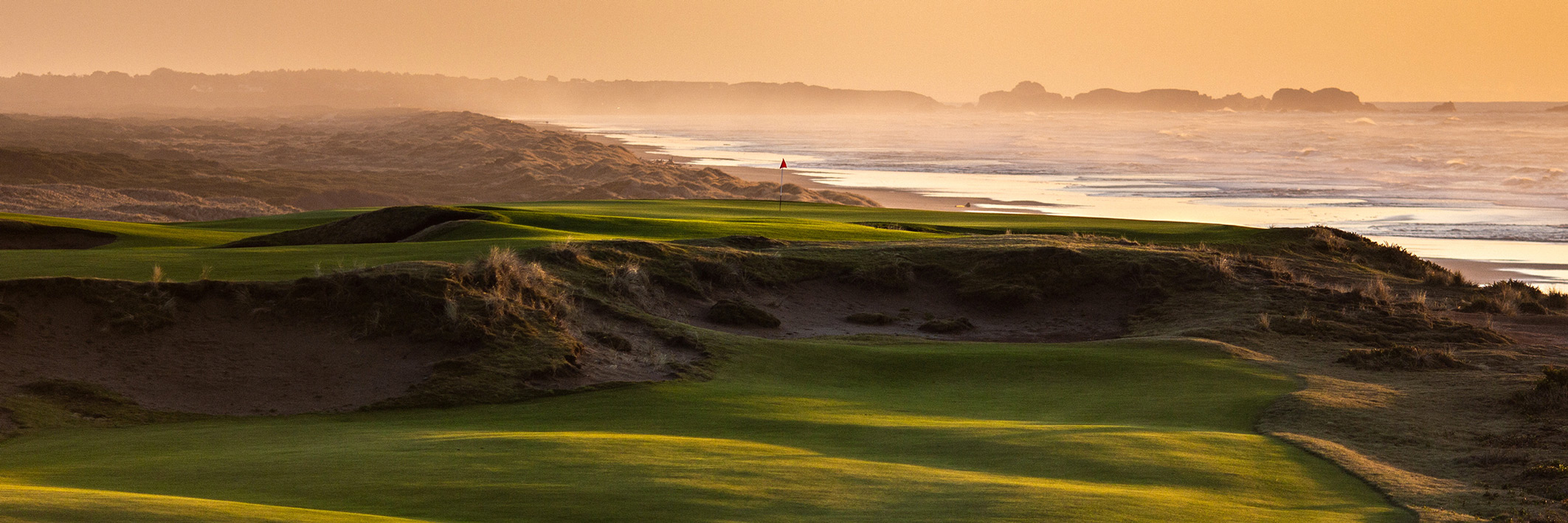 the green of a rugged golf course with view of ocean