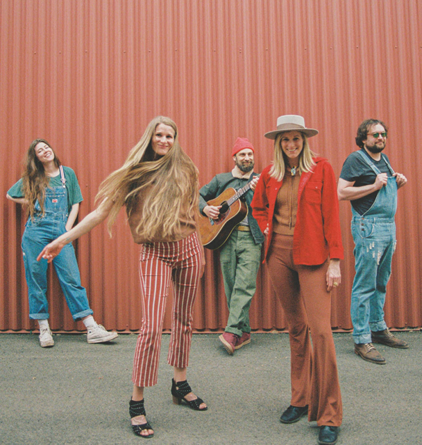 Five people standing in front of a vertical red corrugated metal wall, showcasing casual and retro-inspired fashion styles.