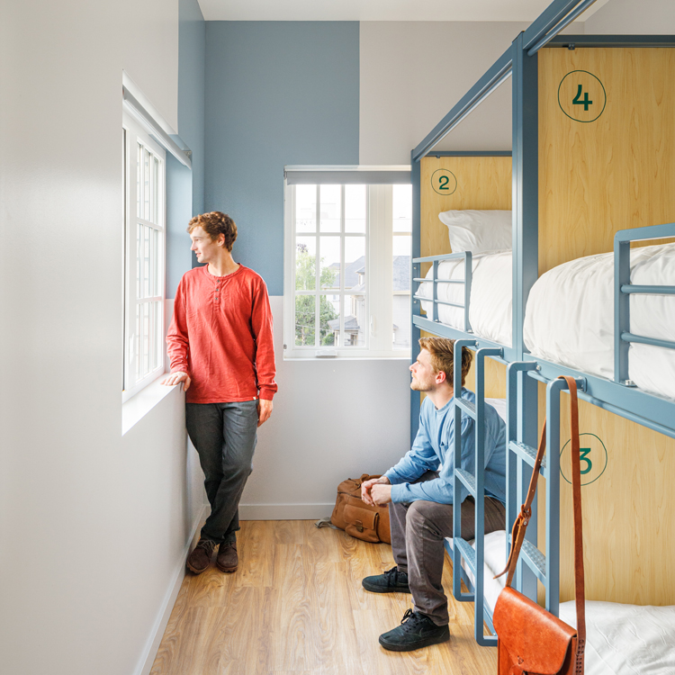 two travellers in dorm style room looking out window
