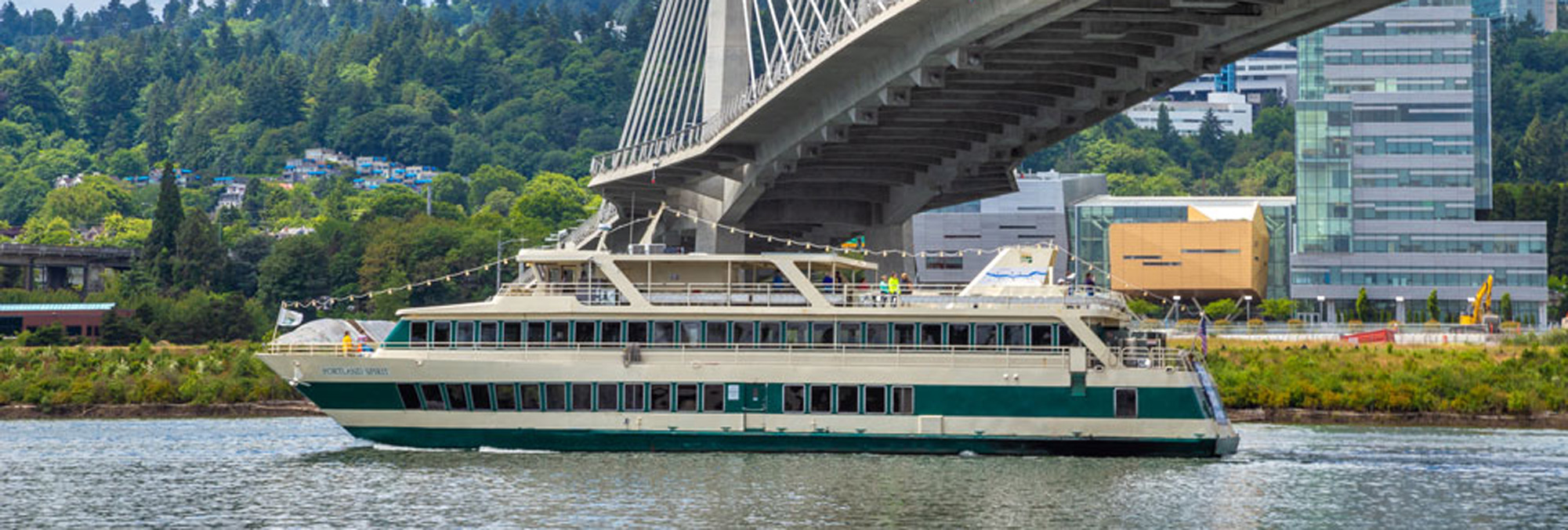 double decked boat floats on water beneath a bridge