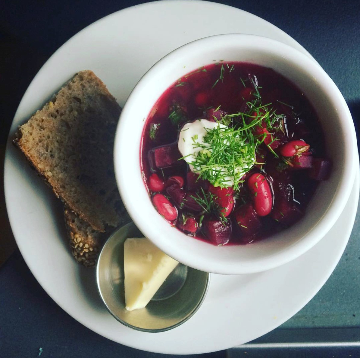 Bowl of red beet soup with sour cream and herbs.