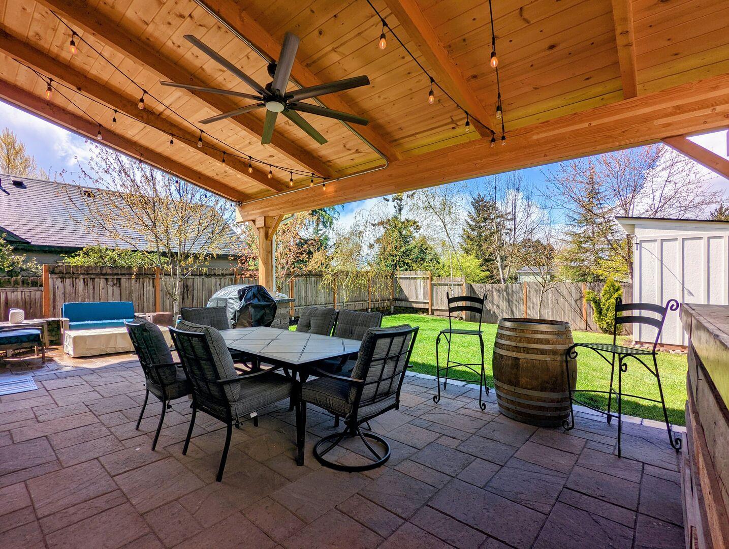 A covered outdoor patio area with a wooden ceiling with a ceiling fan.