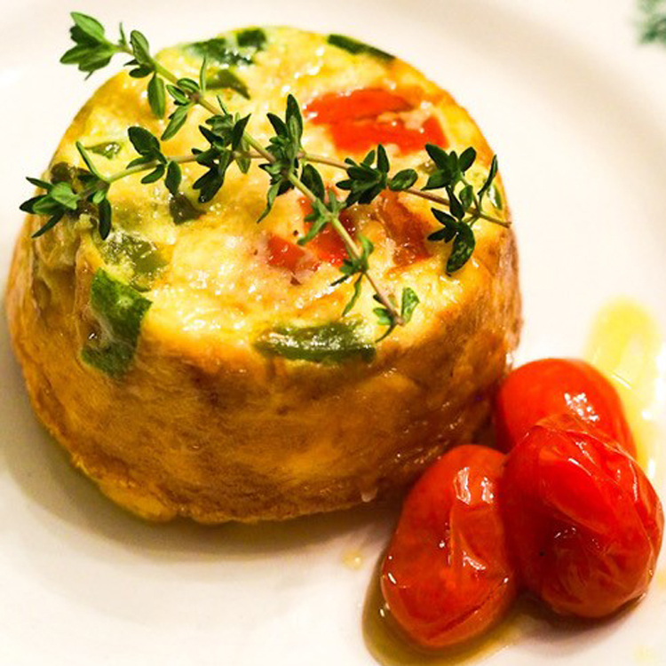 muffin sized spinach quiche with three cooked cherry tomatoes next to it