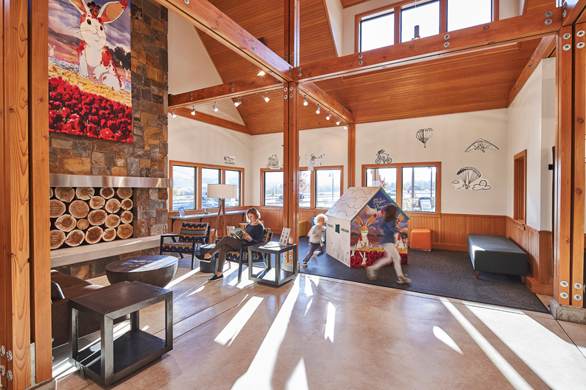two children run around a play house on carpeted area of visitor center