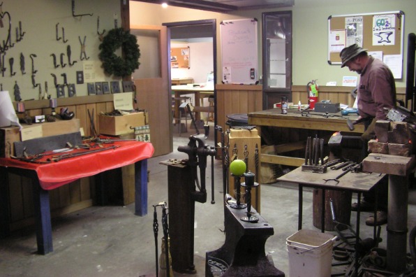 A blacksmith works in an indoor workshop.