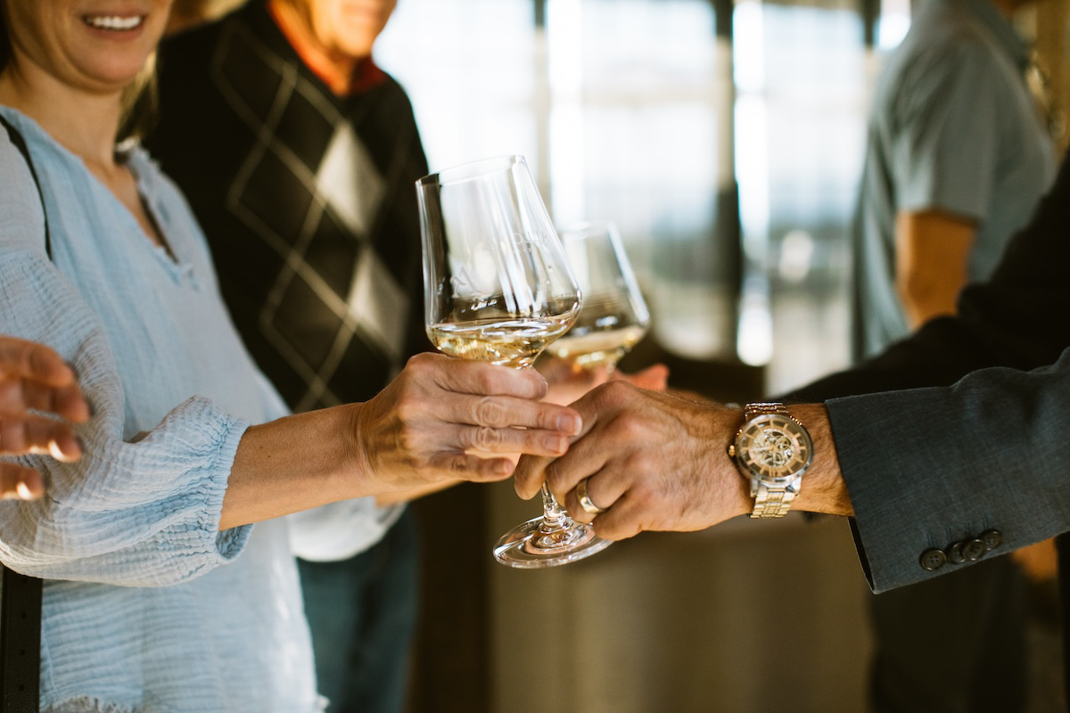 Woman passes glass of white wine to man.