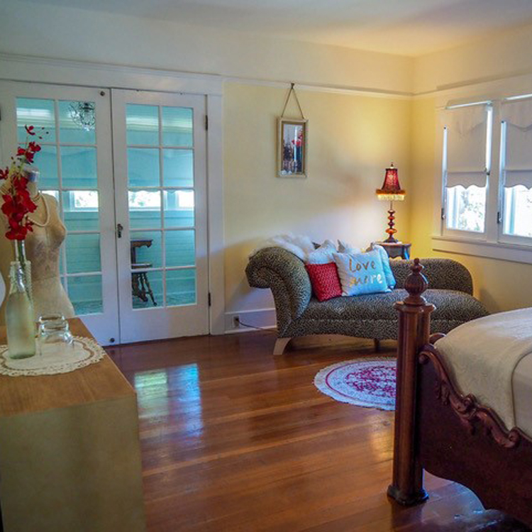 interior of guest room of bed and breakfast with wooden post bed, dresser, fainting couch and door to balcony