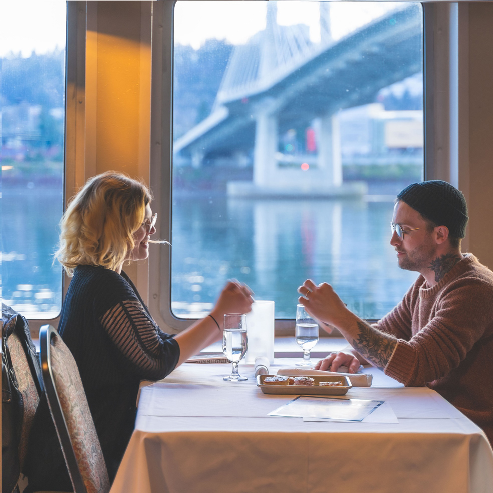 couple dining on yacht with city bridge in background