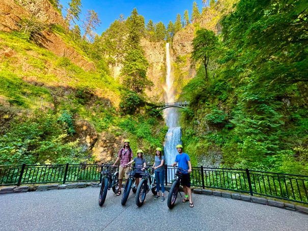 family of four poses next to their bikes in front of tall waterfall