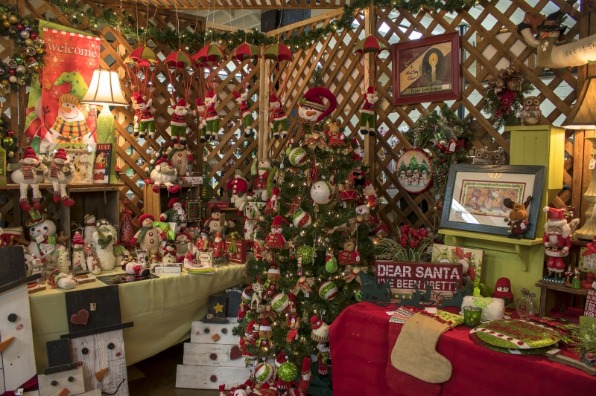 A festive Christmas display inside a wooden lattice booth filled with holiday decorations and ornaments.