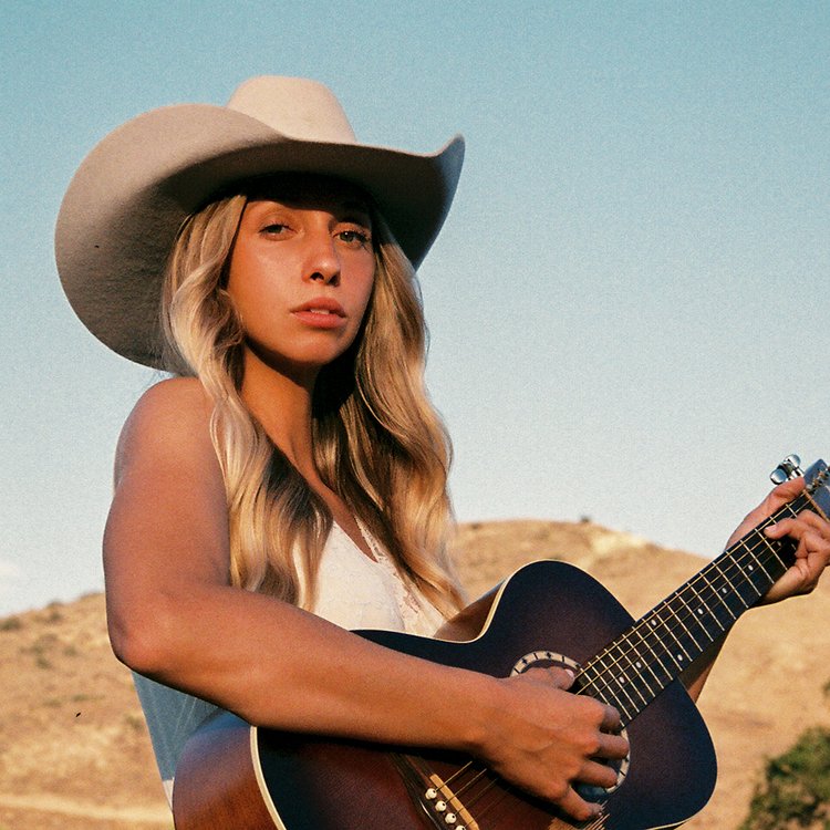woman wearing cowboy hat holds acoustic guitar