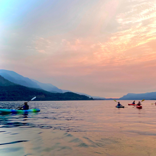 kayakers on large body of water at sunset