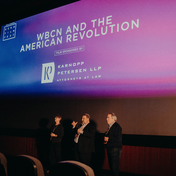three speakers facing audience of movie theater with screen behind them for Bend Film Fest: WBCN and the American Revolution