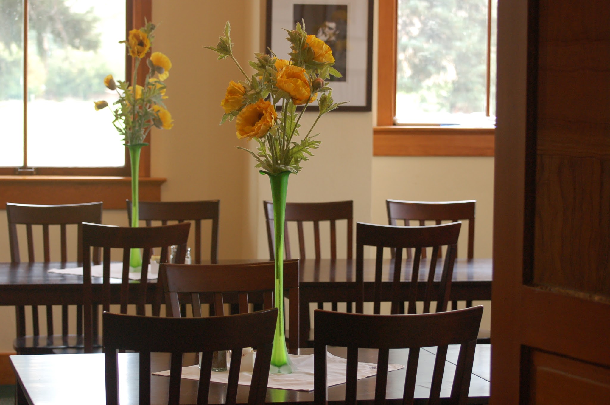 two tables with orange flowers in vases for centerpieces with four chairs at each table