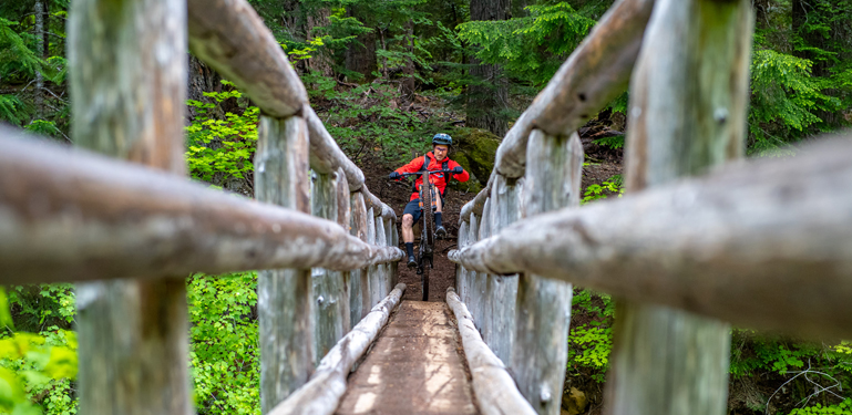 mountain biker pops a wheelie riding on narrow bridge