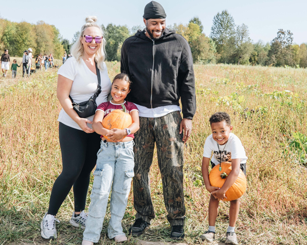 a family of four smiles in a pumpkin patch